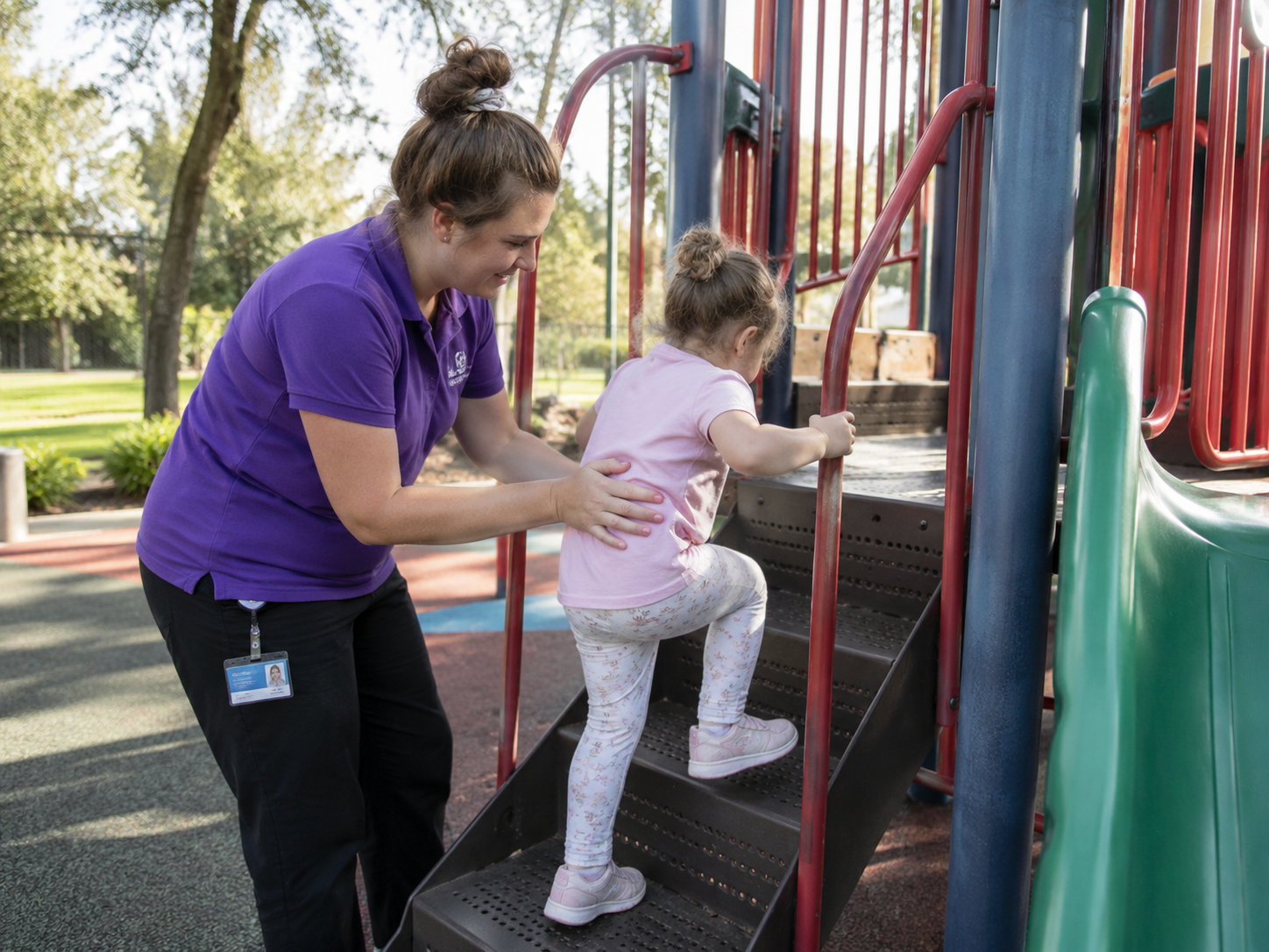 A care worker supporting a young child climbing playground equipment outdoors